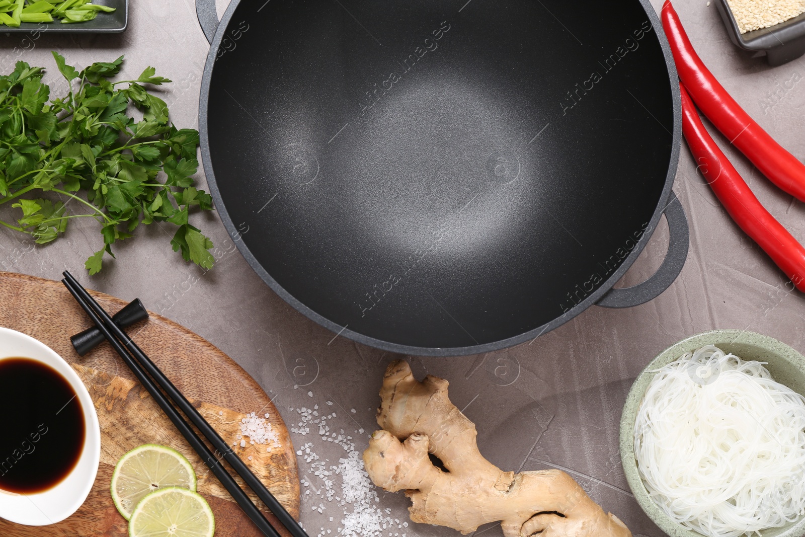 Photo of Wok, chopsticks and different products on grey textured table, flat lay