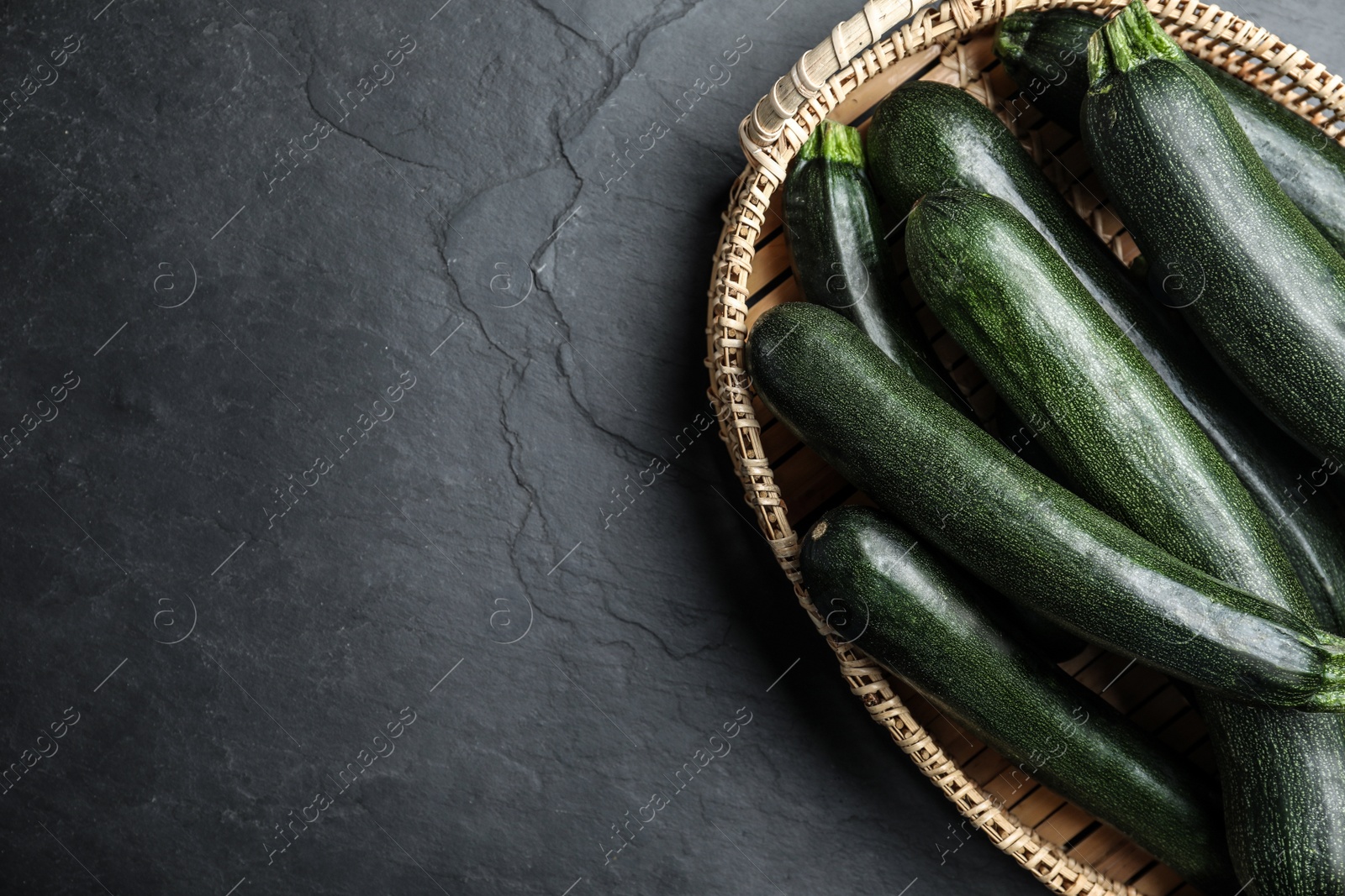 Photo of Basket with green zucchinis on black slate table, top view. Space for text