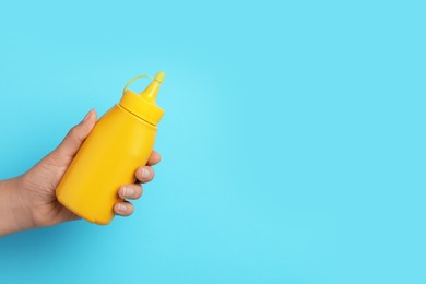 Woman with bottle of mustard on light blue background, closeup. Space for text