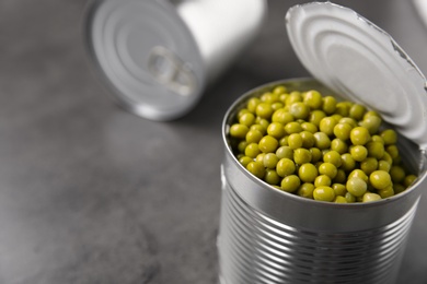 Open tin can with green peas on grey table, closeup. Space for text