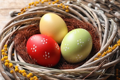 Colorful painted Easter eggs in wicker nest on table, closeup