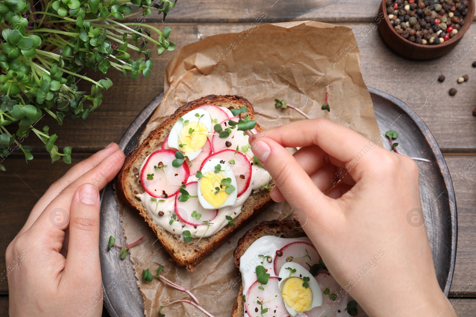 Photo of Woman cooking delicious sandwiches with microgreens at wooden table, top view