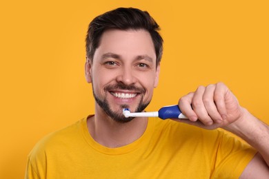 Photo of Happy man holding electric toothbrush on yellow background