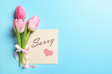 Card with word Sorry and bouquet of tulips on light blue background, flat lay. Space for text