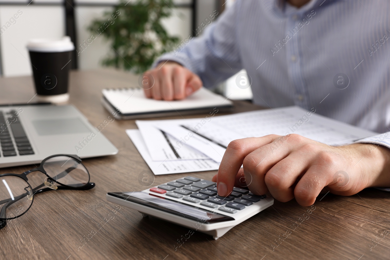 Photo of Man using calculator at wooden table indoors, closeup