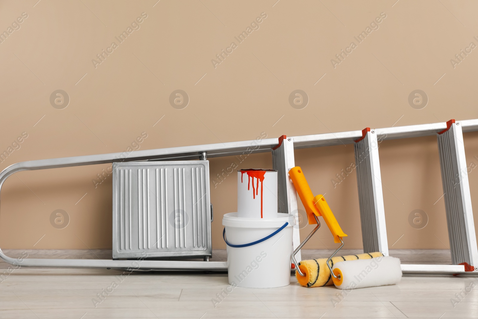 Photo of Metallic folding ladder and painting tools near beige wall indoors