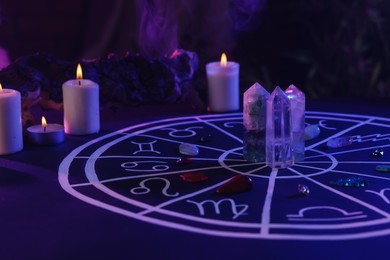 Photo of Natural stones for zodiac signs, drawn astrology chart and burning candles on dark blue table. Color tone effect