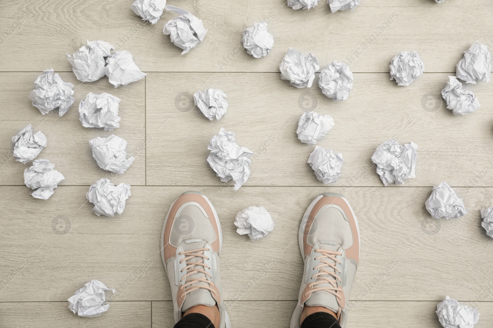 Photo of Closeup of person's feet surrounded by crumpled paper on floor, top view. Lack of ideas