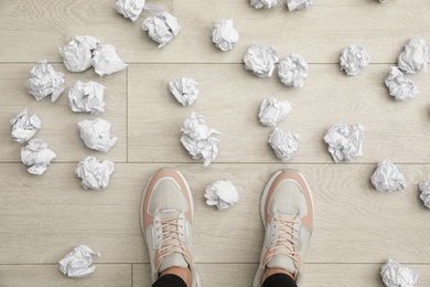 Photo of Closeup of person's feet surrounded by crumpled paper on floor, top view. Lack of ideas