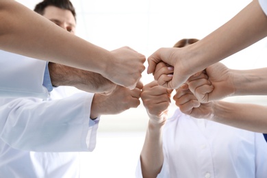 Team of medical doctors putting hands together on light background, closeup. Unity concept