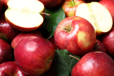 Pile of tasty red apples with leaves as background, closeup