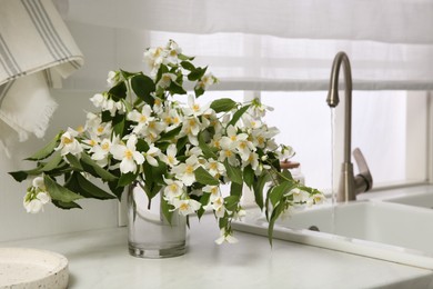 Bouquet of beautiful jasmine flowers in vase on countertop near kitchen sink