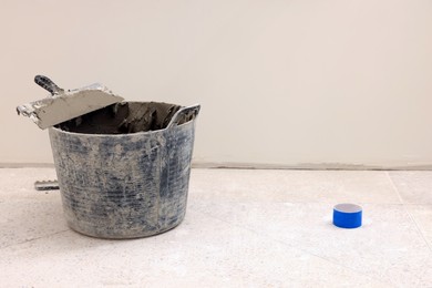 Photo of Bucket of adhesive mix and spatula on floor indoors, space for text. Tiles installation process