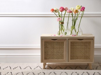 Photo of Beautiful ranunculus flowers on wooden commode near wall in room. Space for text