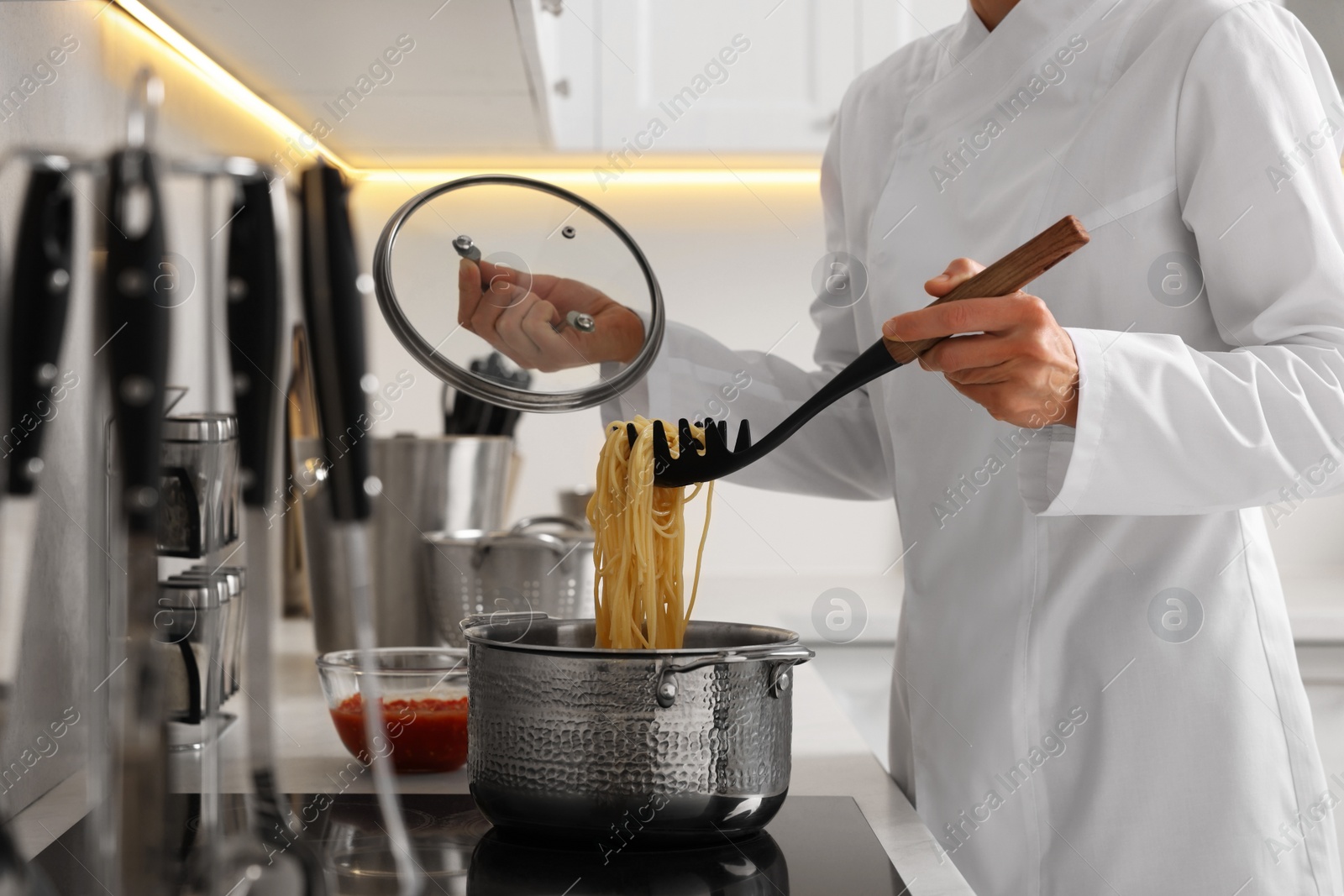 Photo of Professional chef cooking delicious pasta in saucepan indoors, closeup