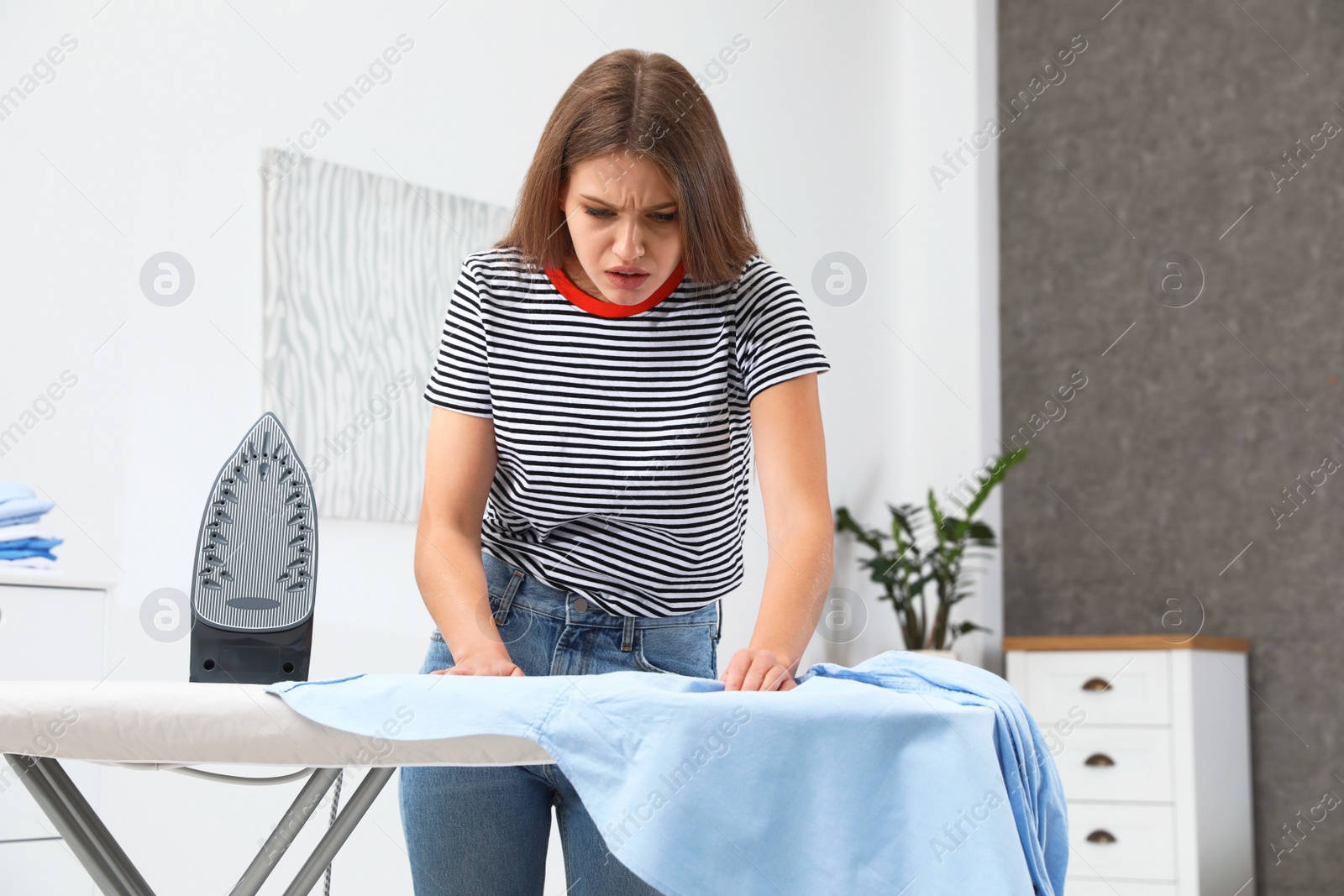 Photo of Emotional woman ironing shirt on board at home