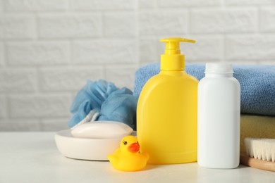 Different baby bath accessories and cosmetic products on white table against brick wall