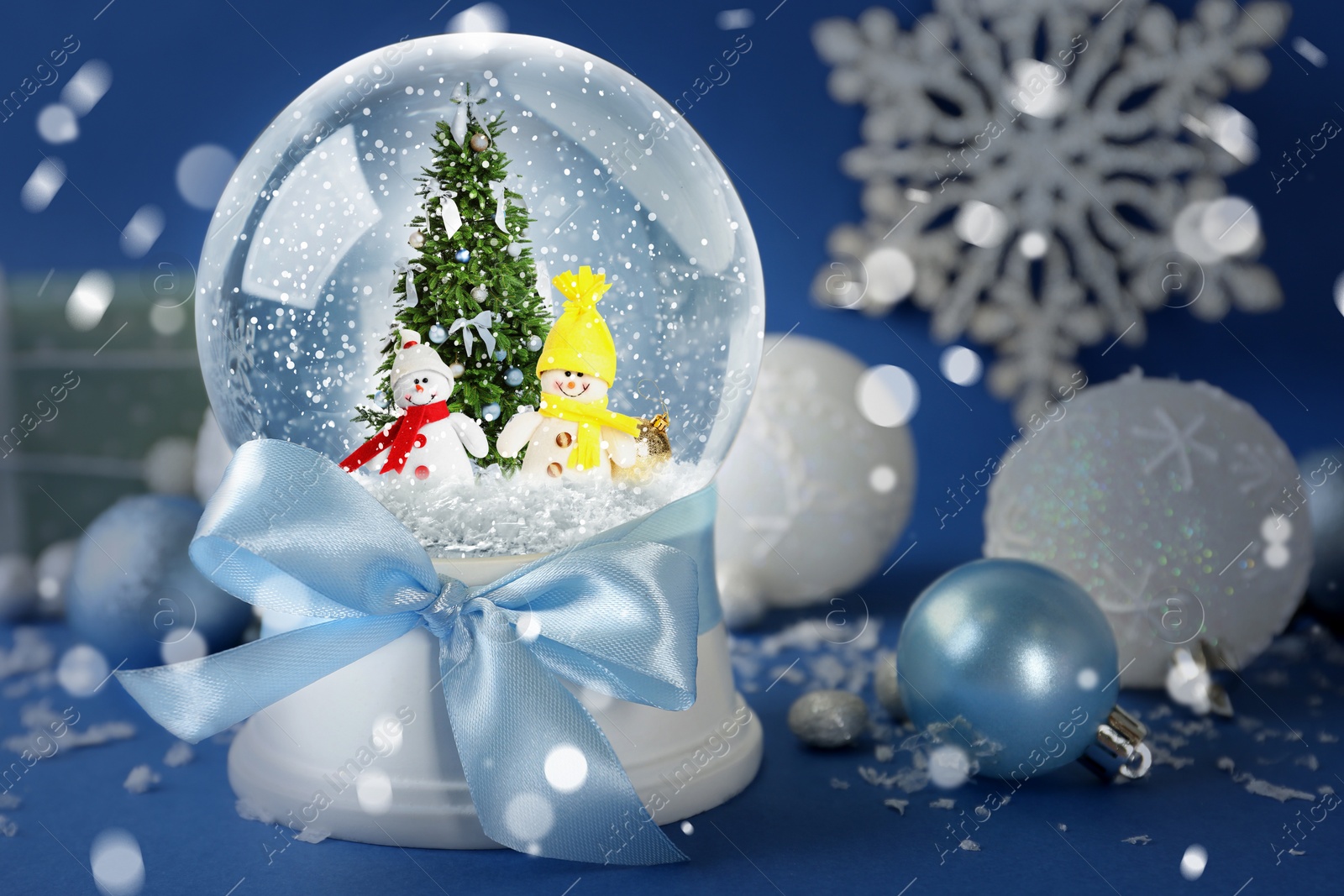 Image of Beautiful snow globe with snowmen and Christmas tree on blue background. Bokeh effect