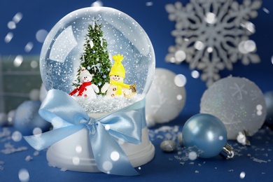 Beautiful snow globe with snowmen and Christmas tree on blue background. Bokeh effect