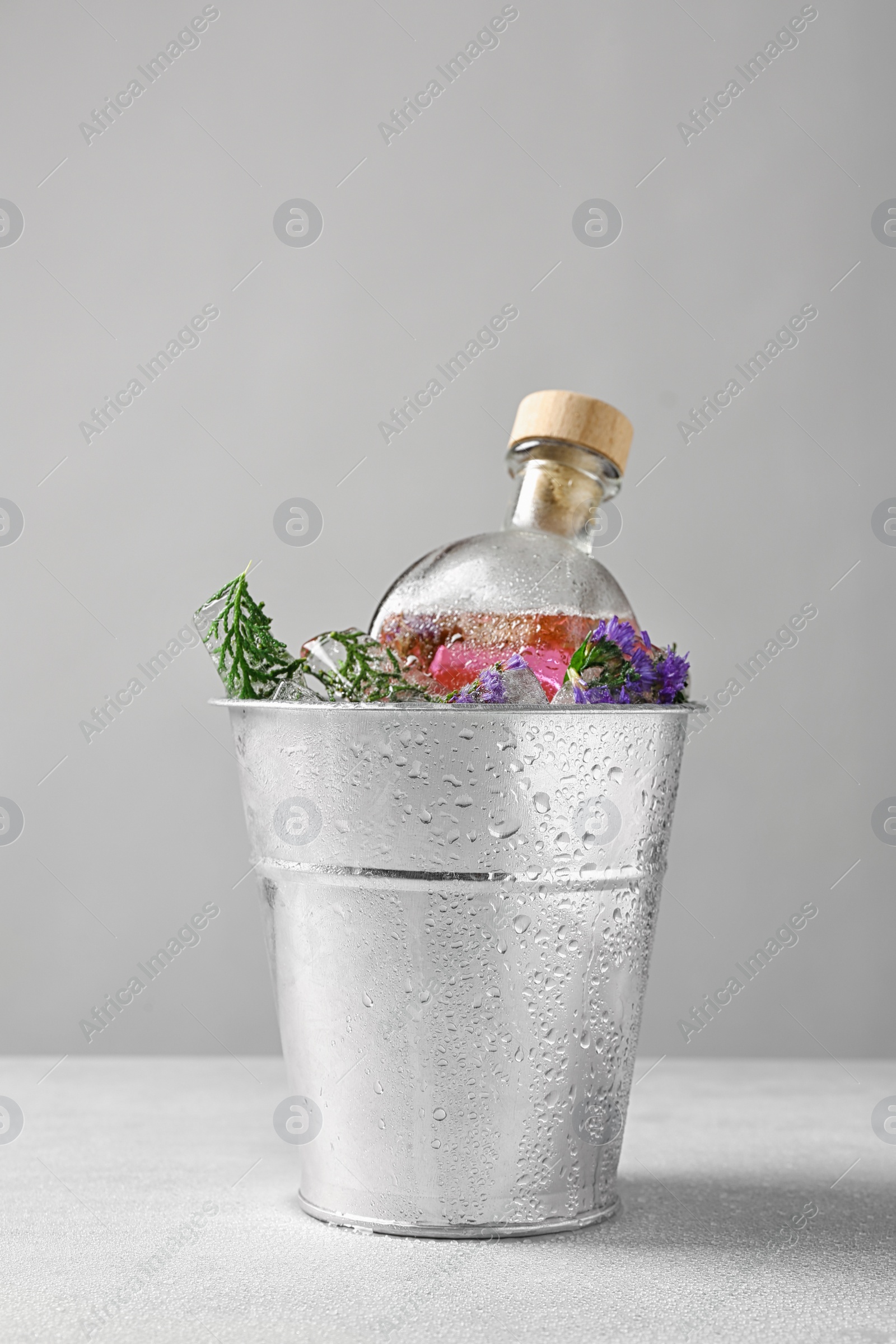 Photo of Bucket of ice cubes with flowers and glass bottle on light table