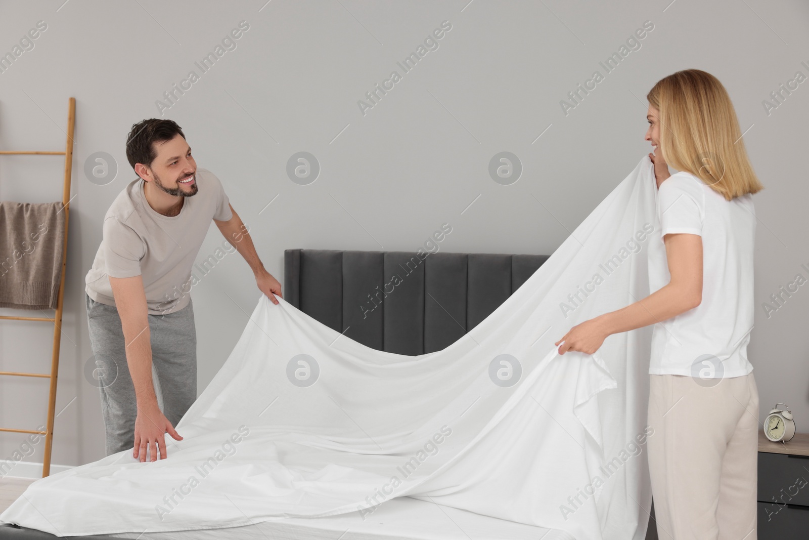 Photo of Couple changing bed linens in room. Domestic chores