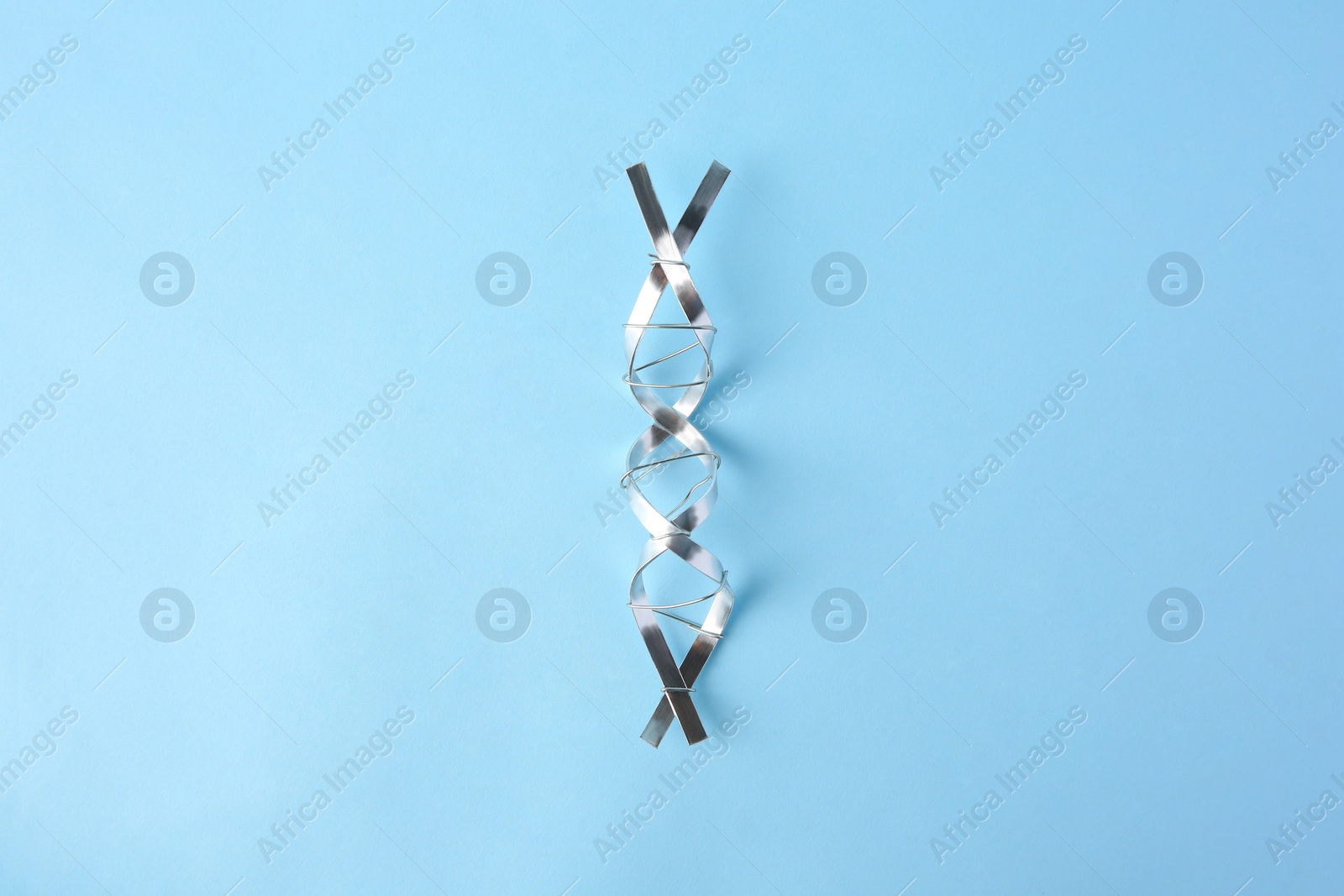 Photo of DNA molecular chain model made of metal on light blue background, top view