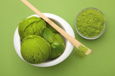 Photo of Tasty matcha ice cream in bowl and bamboo spoon with powder on light green background, flat lay