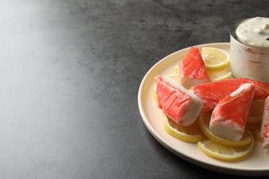 Photo of Delicious crab sticks with lemon slices and sauce on grey table. Space for text