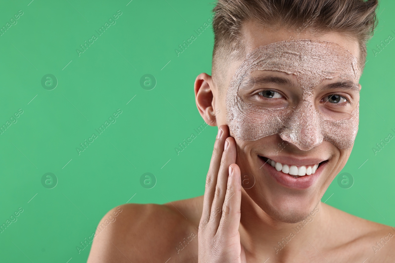 Photo of Handsome man applying facial mask onto his face on green background. Space for text