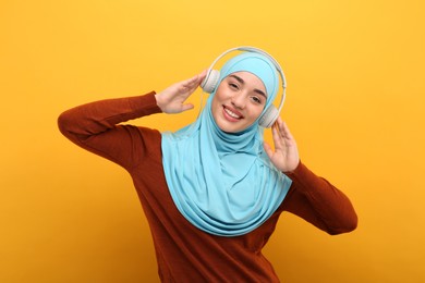 Photo of Muslim woman in hijab and headphones listening to music on orange background
