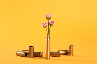 Photo of Bullet cartridge cases and beautiful chrysanthemum flowers on yellow background