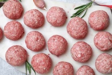 Photo of Many fresh raw meatballs and rosemary on white board, flat lay