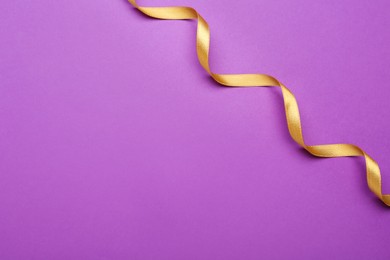Photo of Beautiful golden ribbon on purple background, top view. Space for text
