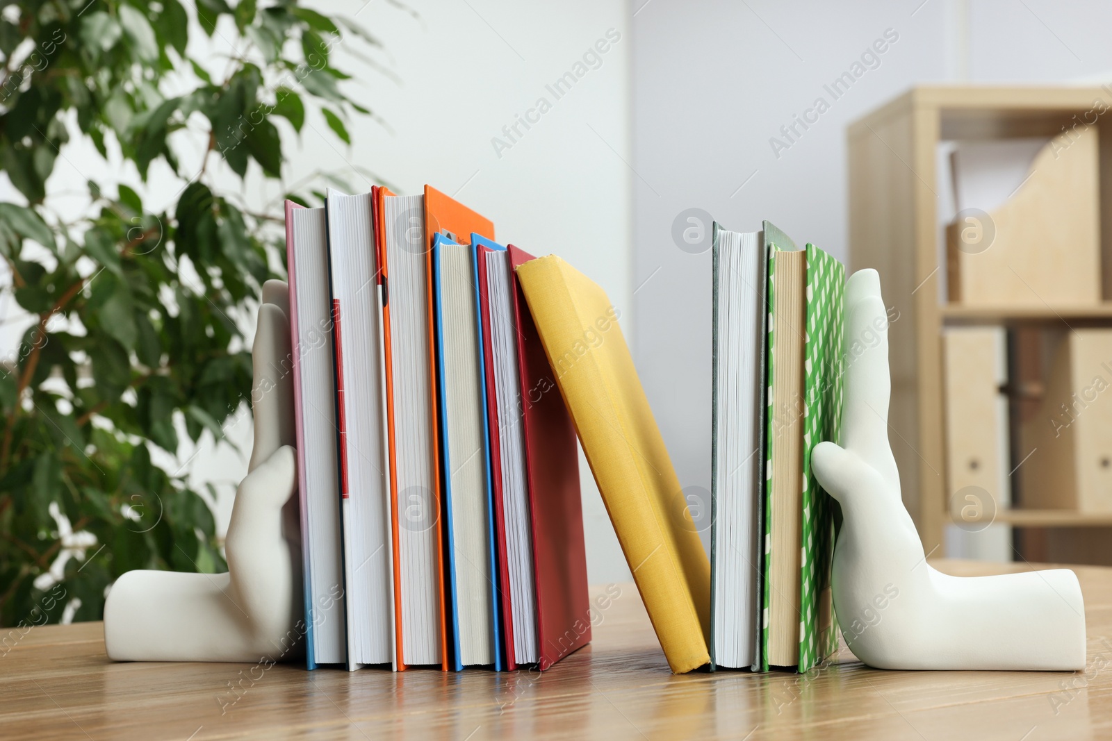 Photo of Beautiful hand shaped bookends with books on wooden table indoors
