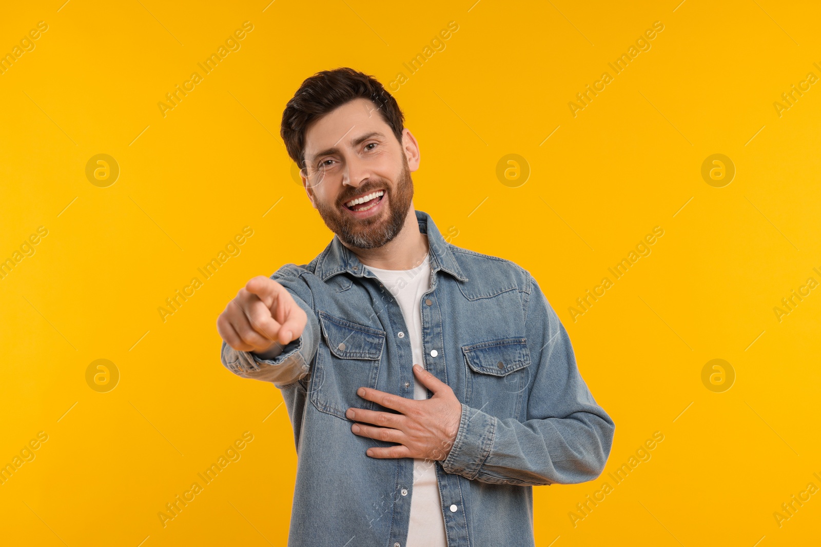 Photo of Handsome man pointing at something and laughing on yellow background