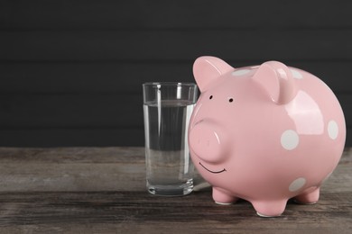 Photo of Water scarcity concept. Piggy bank and glass of drink on wooden table, space for text