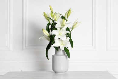 Photo of Beautiful bouquet of lily flowers in vase on light table near white wall