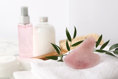 Photo of Rose quartz gua sha tool, cosmetic products and towel on table