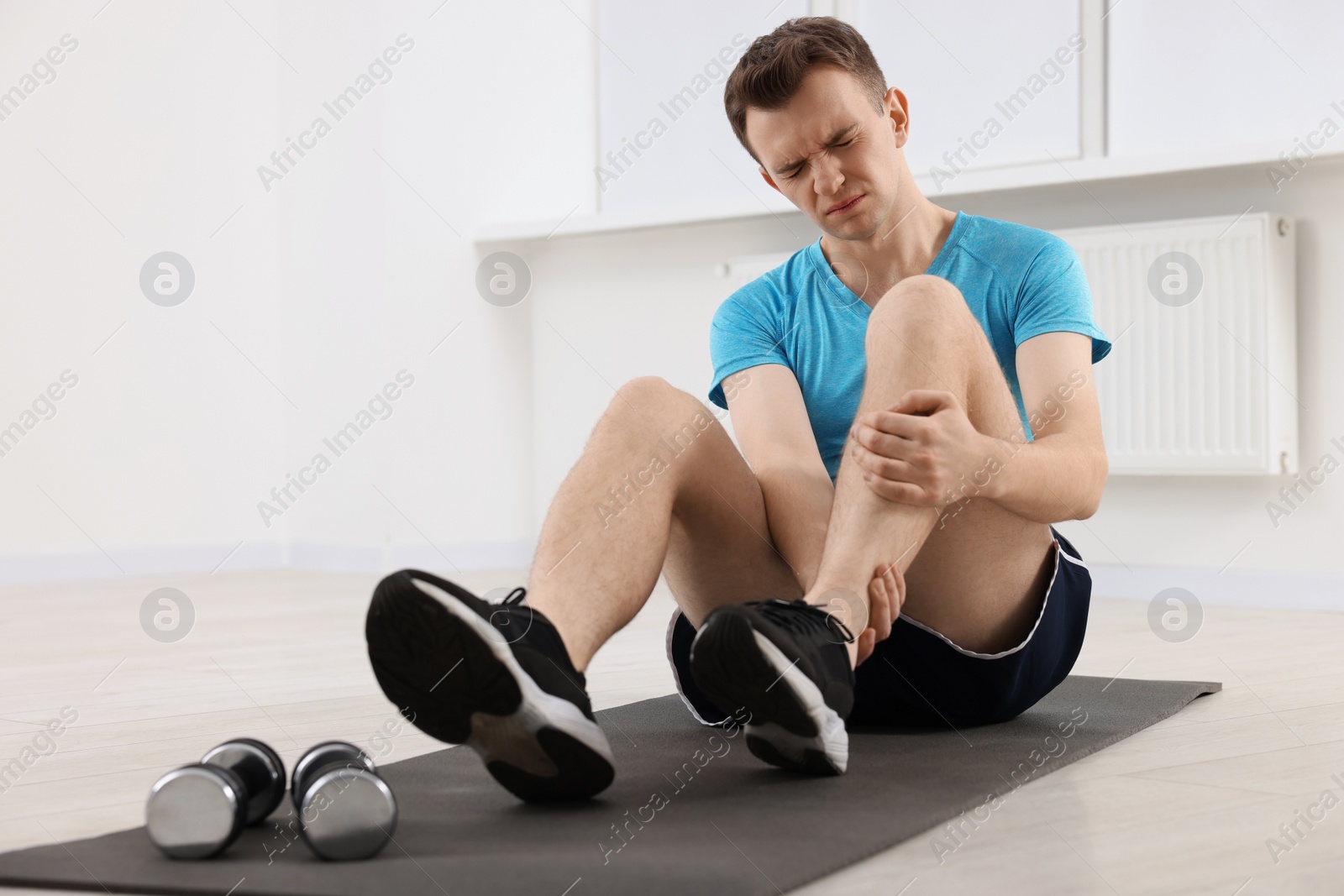 Photo of Man suffering from leg pain on mat indoors
