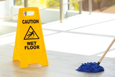 Photo of Safety sign with phrase Caution wet floor and mop, indoors. Cleaning service