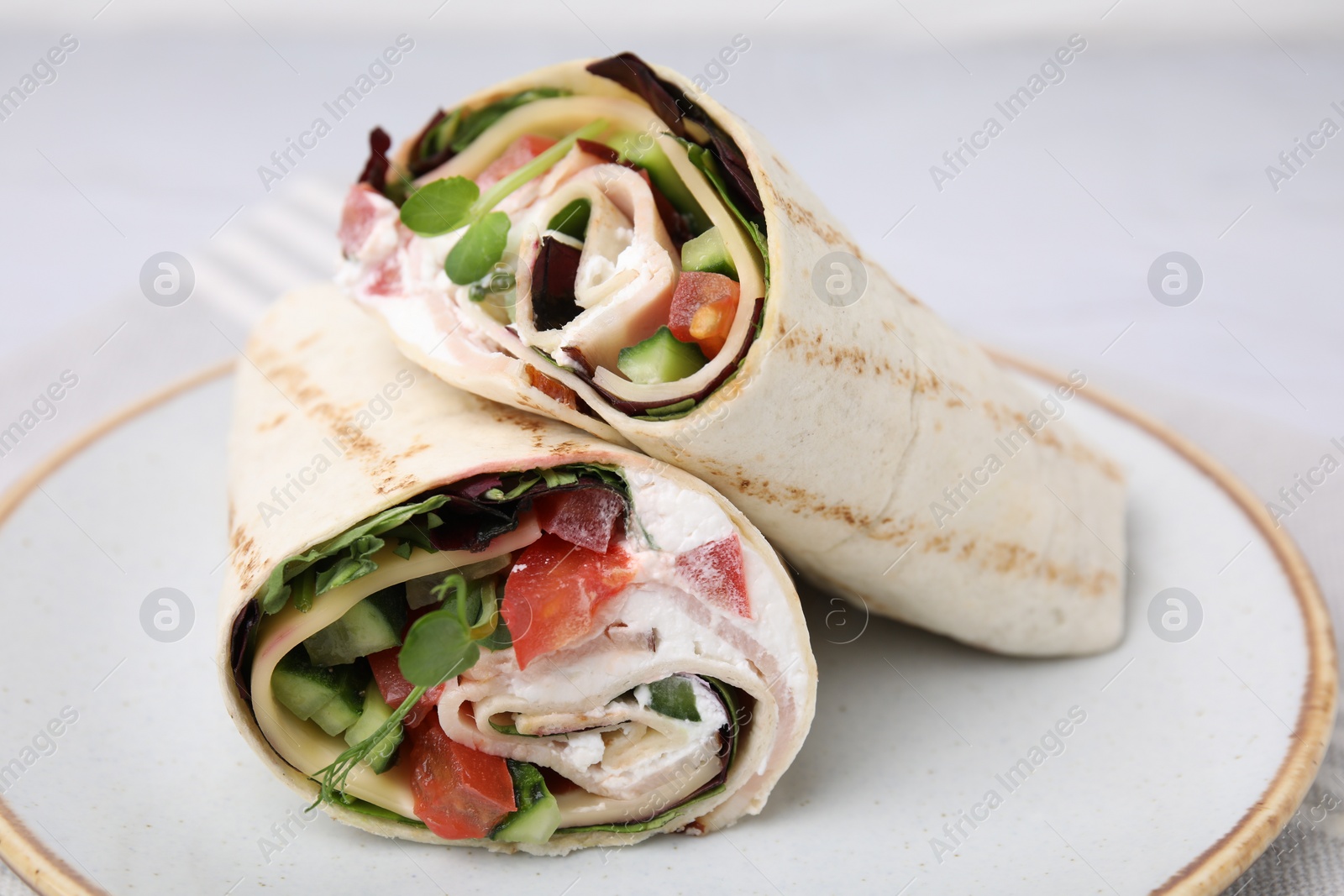 Photo of Delicious sandwich wraps with fresh vegetables on white plate, closeup