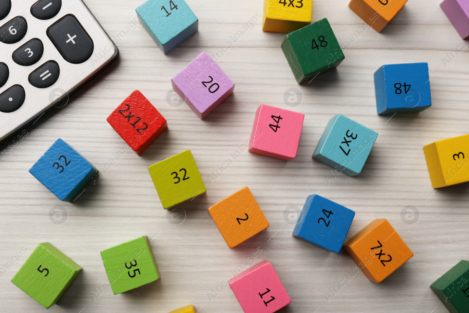 Photo of Colorful cubes with numbers and multiplications near calculator on white wooden table, flat lay