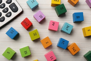 Colorful cubes with numbers and multiplications near calculator on white wooden table, flat lay