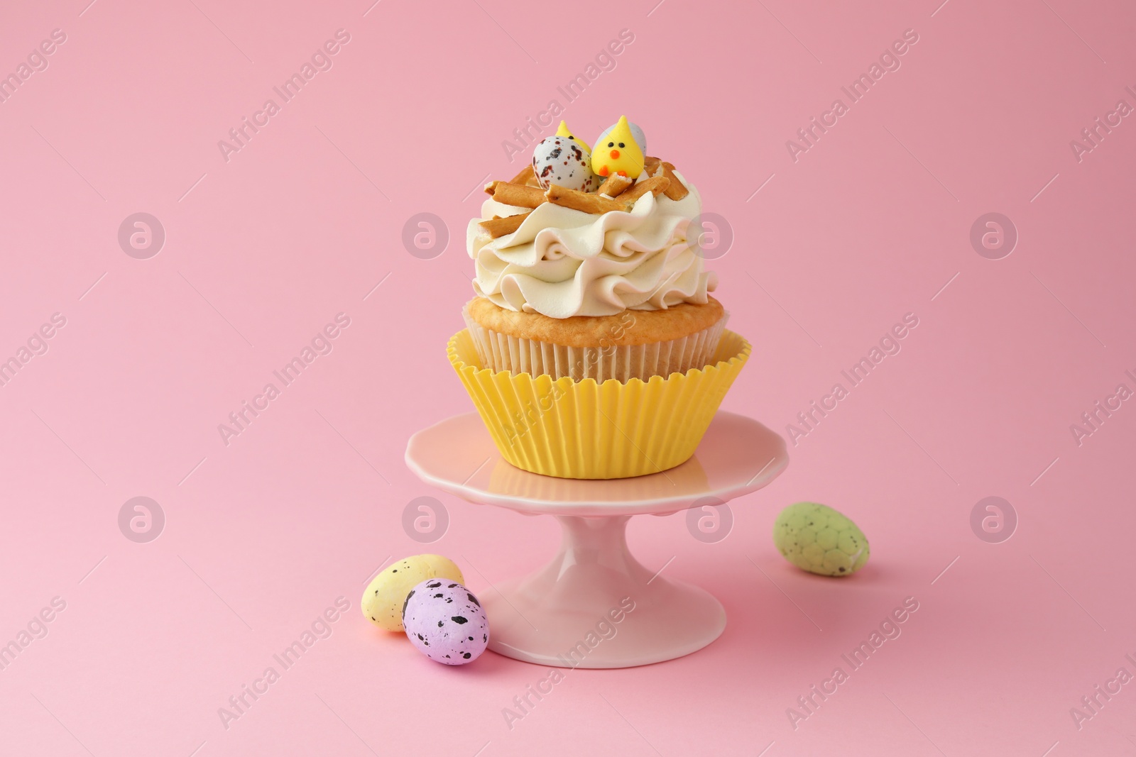 Photo of Tasty Easter cupcake with vanilla cream and candies on pink background