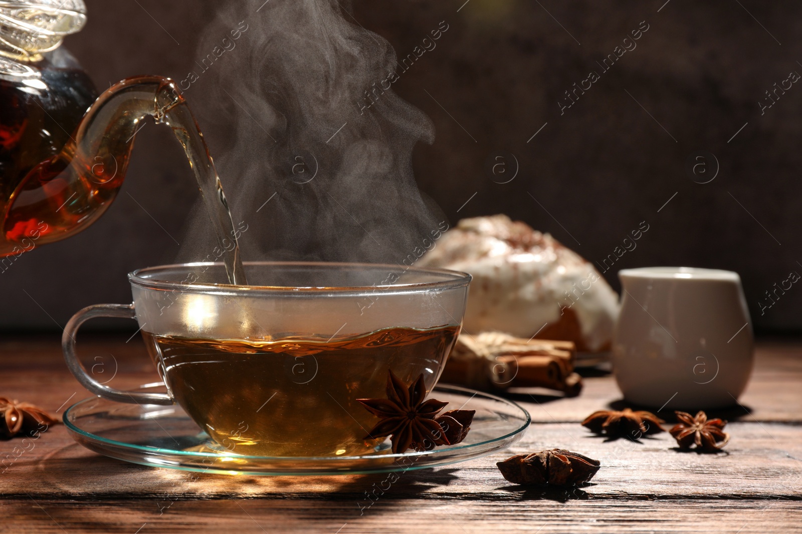 Photo of Pouring aromatic anise tea into glass cup on wooden table