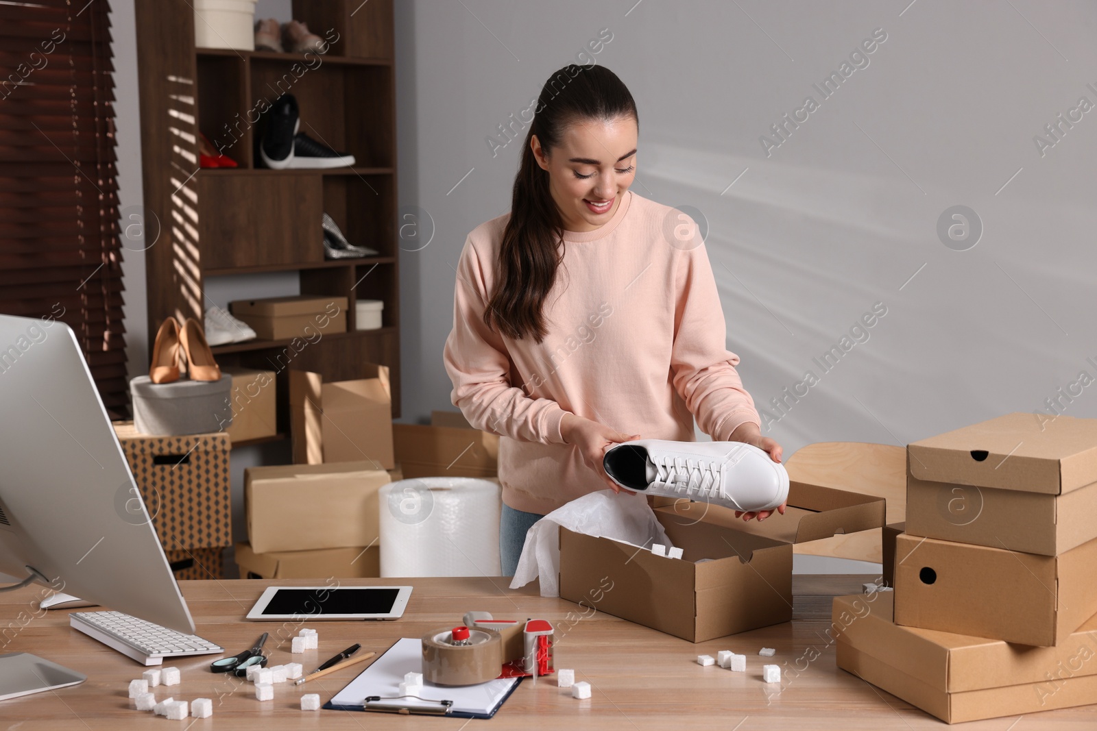 Photo of Seller packing shoes into cardboard box at table in office. Online store