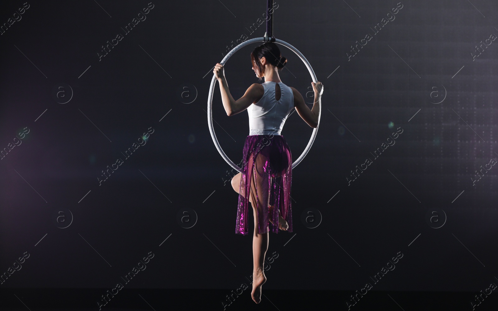 Photo of Young woman performing acrobatic element on aerial ring indoors