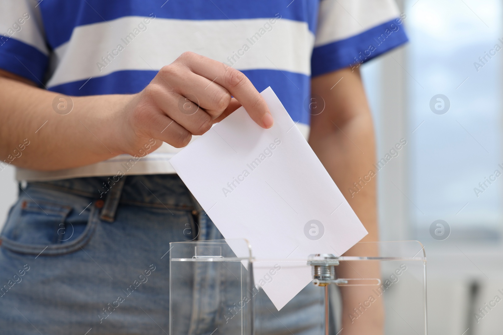 Photo of Woman putting her vote into ballot box on blurred background, closeup