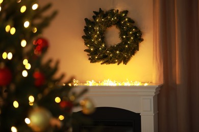 Photo of Beautiful Christmas wreath hanging over fireplace indoors. Bokeh effect