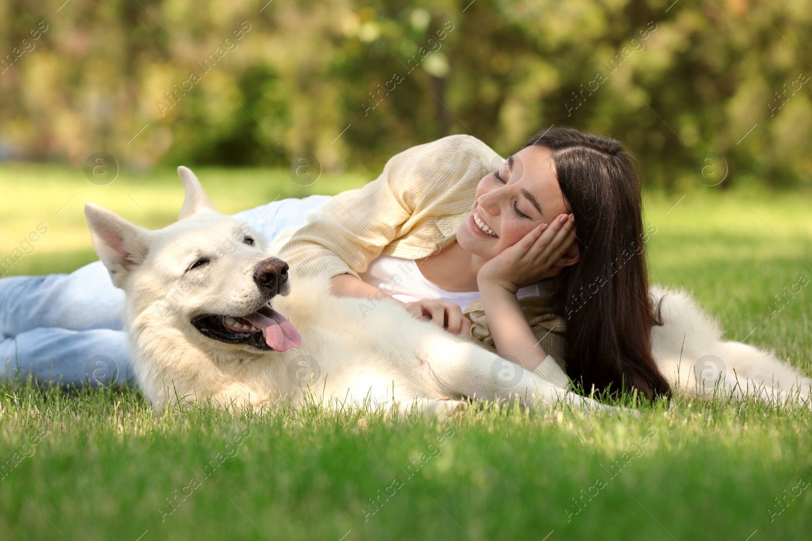 Photo of Teenage girl lying with her white Swiss Shepherd dog on green grass in park